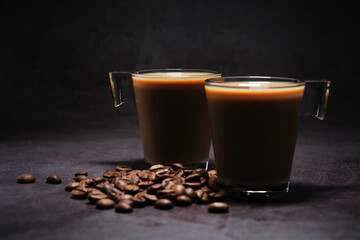 two cups of coffee with milk and scattered coffee beans