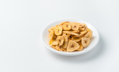 Pieces of dried bananas in a white plate on a light background. Banana chips.