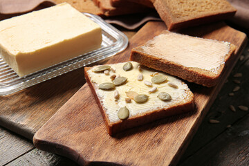Slices of fresh bread with butter and pumpkin seeds on wooden background, closeup