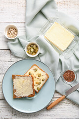 Slices of fresh bread with butter and seeds on light wooden background
