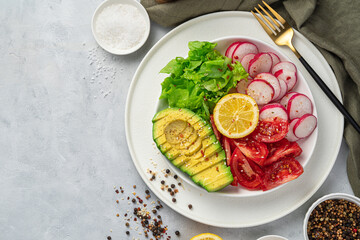 Fresh, summer salad with avocado, tomato and radish on a gray table. Top view, copy space.