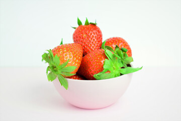 Strawberries in a bowl, presented on a light background. Copy space.