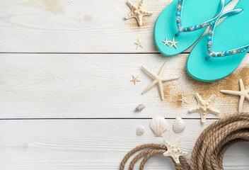 Sea background with seashells, rope and summer flip flops on a white wooden background.