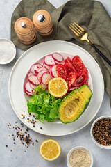 Fresh vegetable salad with avocado, radish, tomatoes, lettuce and sesame on a gray background.