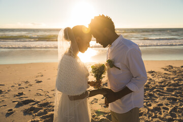 Happy african american couple in love getting married, touching foreheads on beach during sunset