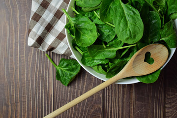 Healthy food. Spinach leaves, in a white bowl and on a checkered cloth, wooden spoon. Zenith view....