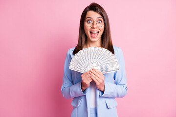 Photo portrait of screaming excited woman holding cash fan isolated on pastel pink colored...