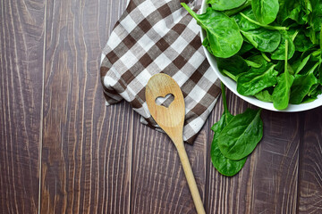 Healthy food. Spinach leaves, in a white bowl and on a checkered cloth, wooden spoon. Zenith view. Copy space.