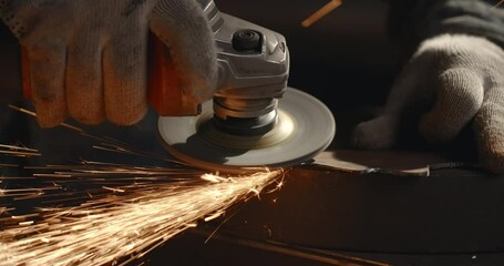 Locksmith sands the edges of a metal detail by electric grinder with a lot of sparks in slow motion, metalwork at workshop, 4k 60p Prores HQ