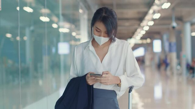 Asian business girl use smart phone for check in boarding pass walk with luggage to terminal at domestic flight at airport. Business commuter covid pandemic, Business travel social distancing concept.