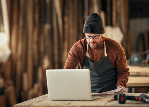Craftsman working with laptop and papers in workshop