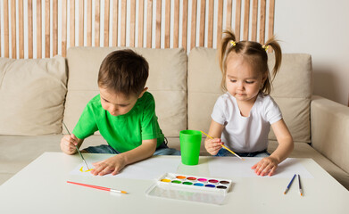little boy and a girl draw with a brush and paint on paper at a table in a room