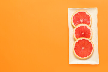 Plate with slices of ripe grapefruit on color background
