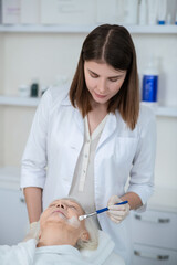 Cosmetologist applying moisturizing mask on the womans face