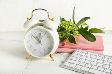 Alarm clock, computer keyboard and notebooks on light background