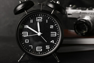 Alarm clock, notebooks and photo camera on dark background, closeup