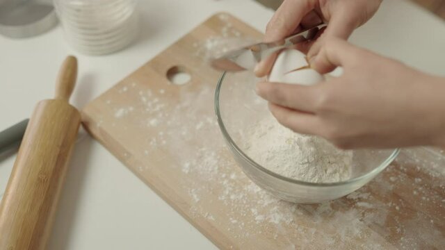 Cook cracking egg into bowl of flour slow-mo, homemade food preparation, pastry