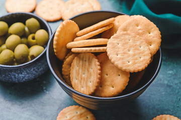 Bowl of crackers and olives on color background