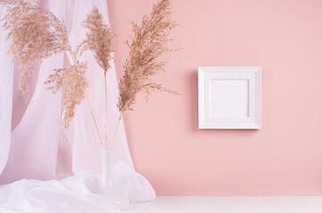 Calm home decor with square blank photo frame for text hanging on pink wall, silk curtain, fluffy reeds bouquet on white wood table. Template for display and portfolio.