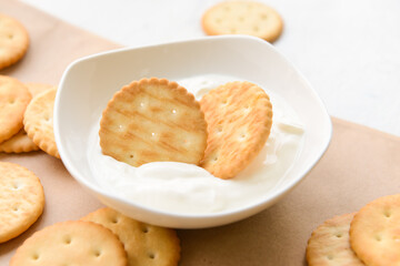 Bowl of crackers with sauce on light background