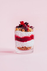 close-up of chia pudding with granola yogurt currants in a transparent glass on a pink background