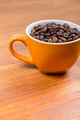 close-up of a orange ceramic cup with white inside with coffee beans on a wooden surface, vertical photo