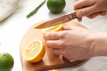 Woman cutting lemon on light background