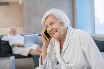 Gray-haired smiling woman looking pleased and talking on the phone