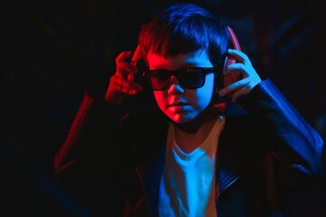 teen boy listening to music with headphones, neon light trending portrait. Looks at the camera