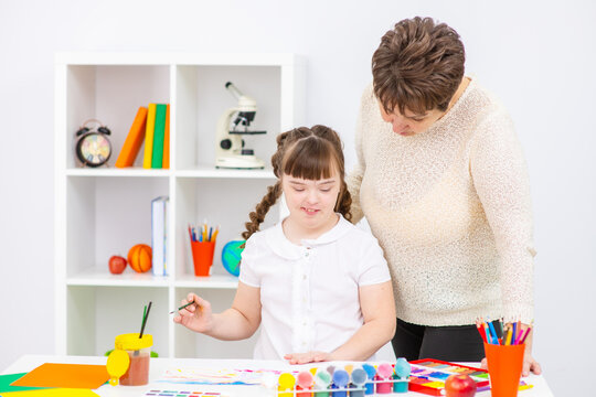 A girl with down syndrome sits next to her mother and is engaged in creativity, drawing a picture in an album. Education for people with disabilities concept