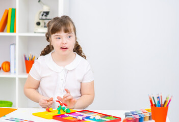 A girl with the syndrome at the table are engaged in creativity. Education for people with disabilities concept