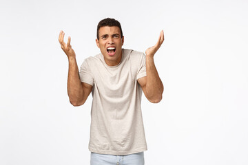 Disappointed and freak-out, bothered handsome man in t-shirt, raising hands up frustrated and...