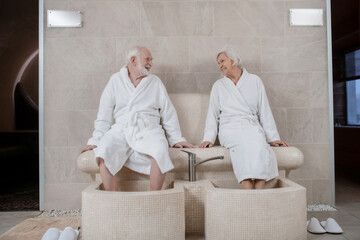 Senior couple in white robes having procedures for legs in spa salon
