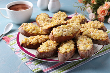 Baked homemade toasts with chicken, cheese, pineapple and garlic on a plate on light blue background.