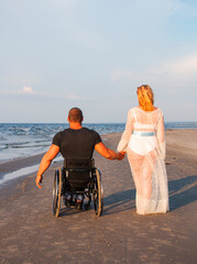 man Young disabled athlete in a wheelchair with his beloved woman in a white dress, on the seashore. Love, love story