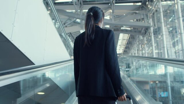 Asian business girl wear face mask drag luggage stand on escalator look around walk to terminal at international airport. Business commuter covid pandemic, Business travel social distancing concept.