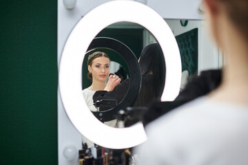 Bride getting ready for wedding. Professional make-up artist applying blush on female clients' face with big makeup brush. Work process in beauty studio. Close-up picture on make-up model.