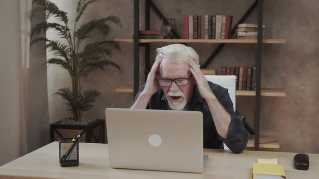 Shocked surprised senior mature man looking at laptop reading unbelievable online news at home