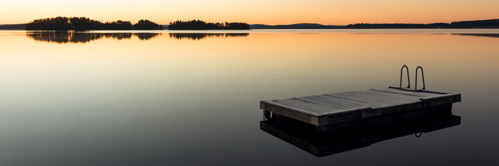 panorama of a wooden raft on calm lake water at sunrise or sunset