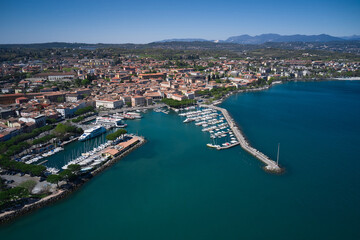 Fototapeta na wymiar Aerial view of the coastline of the city of Desenzano del Garda on Lake Garda, Italy. Aerial panorama of Italian cities. Desenzano del garda port.