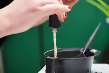 Close-up picture of hairdresser's tools in female hands. Process of squeezing hair dye from tube into plastic bowl. Hair stylist preparing for dying hair in barber shop. Beautification.