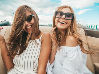 Portrait of two young beautiful and smiling hipster female in convertible car. Sexy carefree women...
