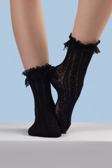 Cropped shot of female legs in black lace socks with knit design and wide lace ruffles on the rims....