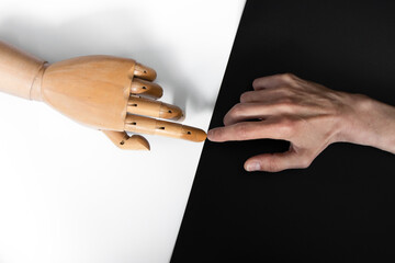 A wooden hand touches a human hand on a white and black background