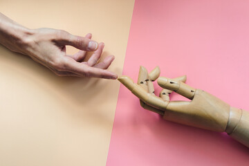 A wooden hand touches a human hand on a beige and pink background