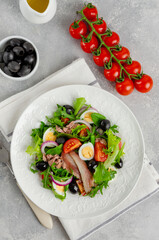 French salad Nicoise with tuna, egg, green beans, tomatoes, olives, lettuce, onions and anchovies on a gray concrete background. Healthy food.