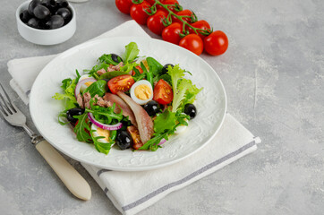 French salad Nicoise with tuna, egg, green beans, tomatoes, olives, lettuce, onions and anchovies on a gray concrete background. Healthy food.