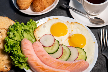 Two fried eggs and sausages, pieces of salad, cucumber and radish on a white plate, toast, croissants and a cup of tea or coffee. Scrambled eggs. Breakfast. Healthy eating. Close-up