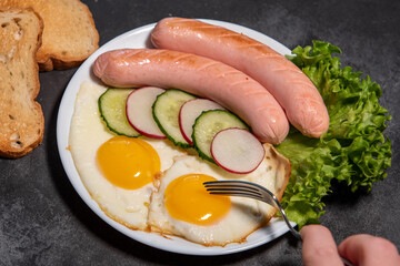 Two fried eggs and sausages, lettuce, cucumber and radish slices on a white plate, toast. Scrambled eggs. Breakfast. Healthy eating. Close-up