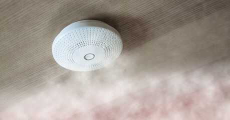 modern smoke detector on wooden ceiling with white smoke and fog, symbol for fire protection and...